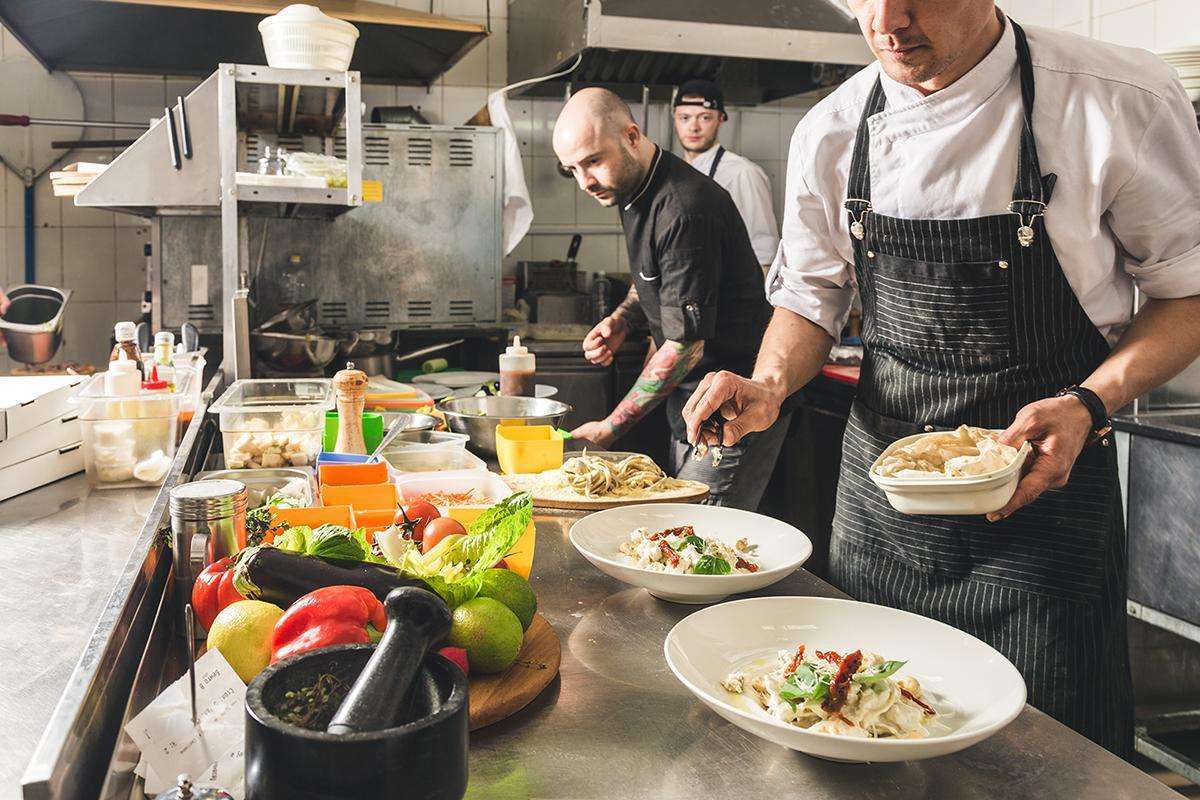 Professional Chef Cooking In The Kitchen Restaurant At The Hotel, Preparing Dinner. A Cook In An Apron Makes A Salad Of Vegetables And Pizza.